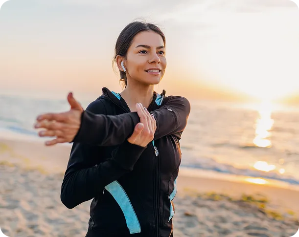 A woman stretching outdoors at sunrise by the shore
