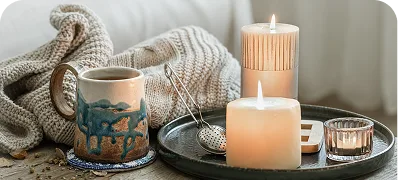 Lit candles and a mug on a tray with a knitted blanket