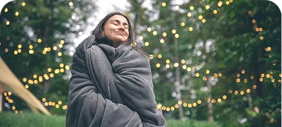 A person wrapped in a blanket outdoors under festoon lights